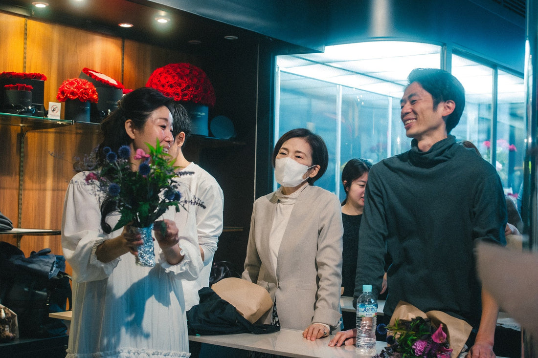 花活JAPANの会場で、花束を持った参加者とテーブルを囲む人たち